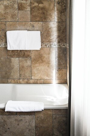 Ein Badezimmer mit einer Badewanne, einem Handtuch an der Wand und einer gefliesten Rückwand.