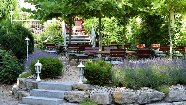 Une terrasse de jardin avec des marches en pierre menant à un espace détente, entouré de lavande et de verdure.
