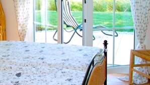 Une chambre avec un lit, une chaise et une vue sur un jardin, accessible par une porte-fenêtre coulissante.