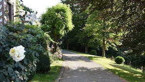 Un chemin de gravier bordé d’une végétation luxuriante et un bâtiment blanc avec une enseigne.