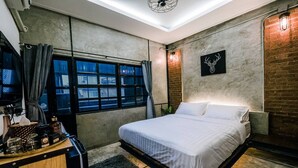 Ein modernes Schlafzimmer mit einem Bett, einem Schreibtisch mit Kaffeemaschine und einem großen Fenster mit Vorhängen.