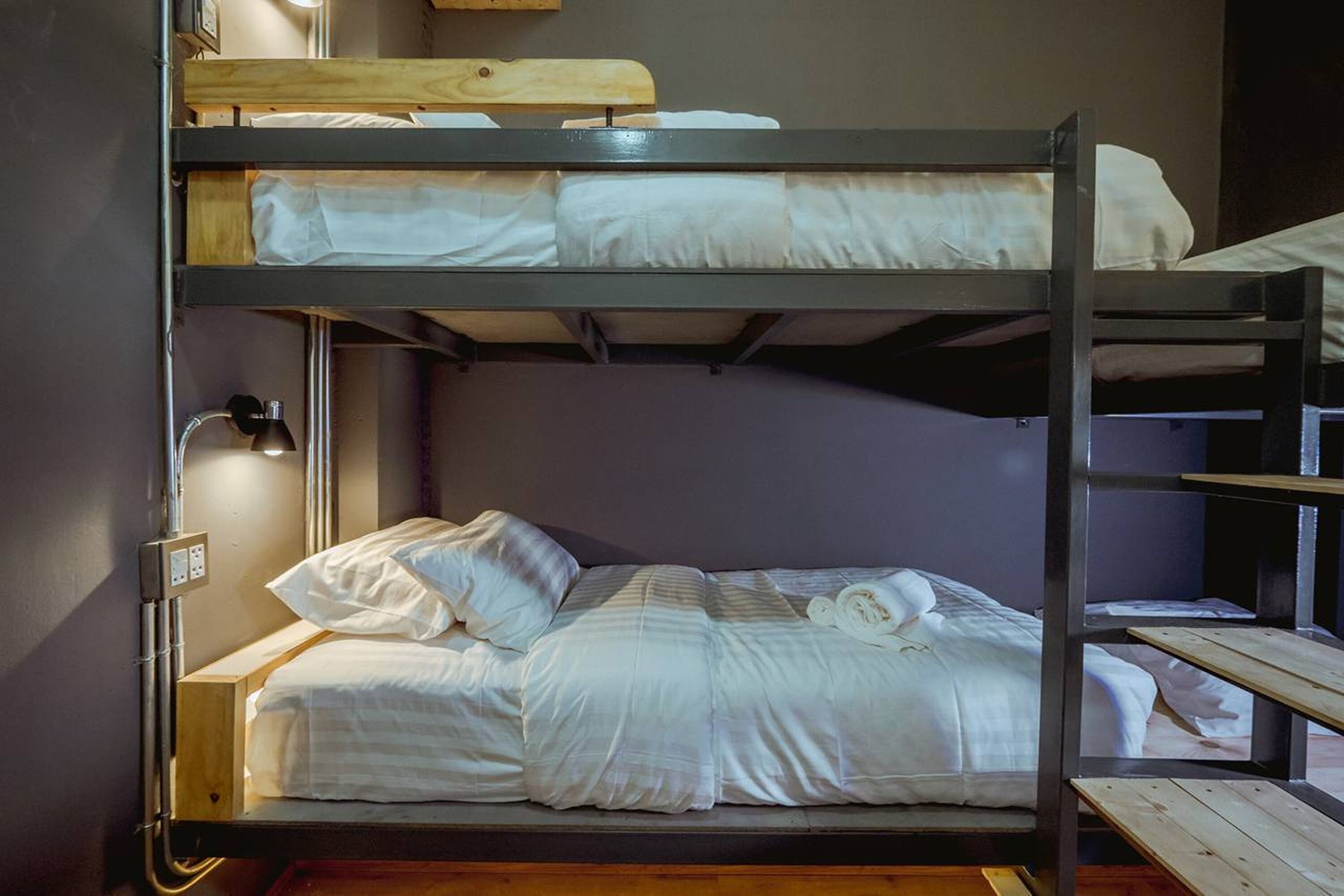 Una cama litera con cabecera de madera, una lámpara de pared y un enchufe.