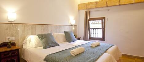 A neatly made bed with pillows, a bedside table with a lamp, and a window with curtains.