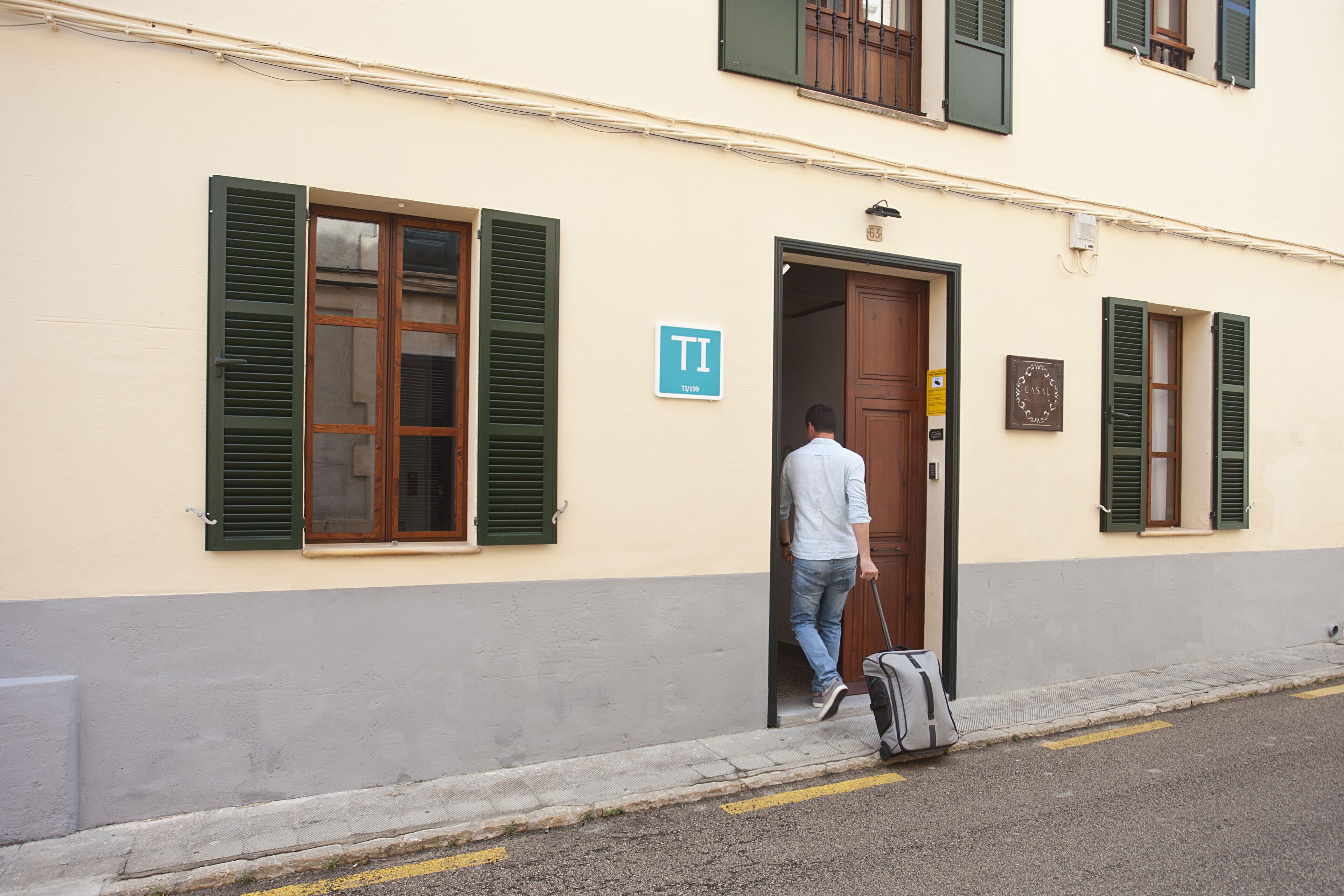 A man exiting a building with a suitcase, a sign with the letter "T" on the wall, and a door with a handle.