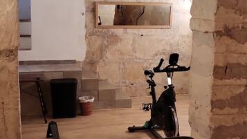An underground gym with exercise equipment, a white wall with a sign, and exposed brick walls.