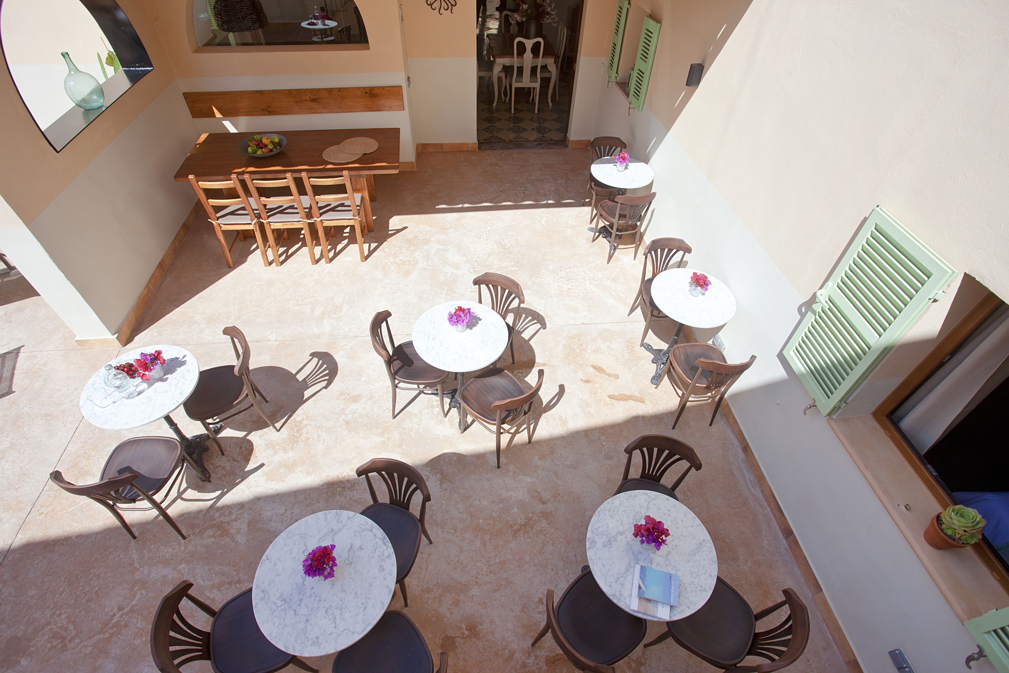 Un patio con varias mesas y sillas redondas, un banco de madera y vista al interior a través de un acceso.