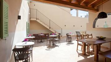 Un espacio de comedor al aire libre con varias mesas y sillas, una escalera que conduce a un nivel superior, y un colgador de luces.
