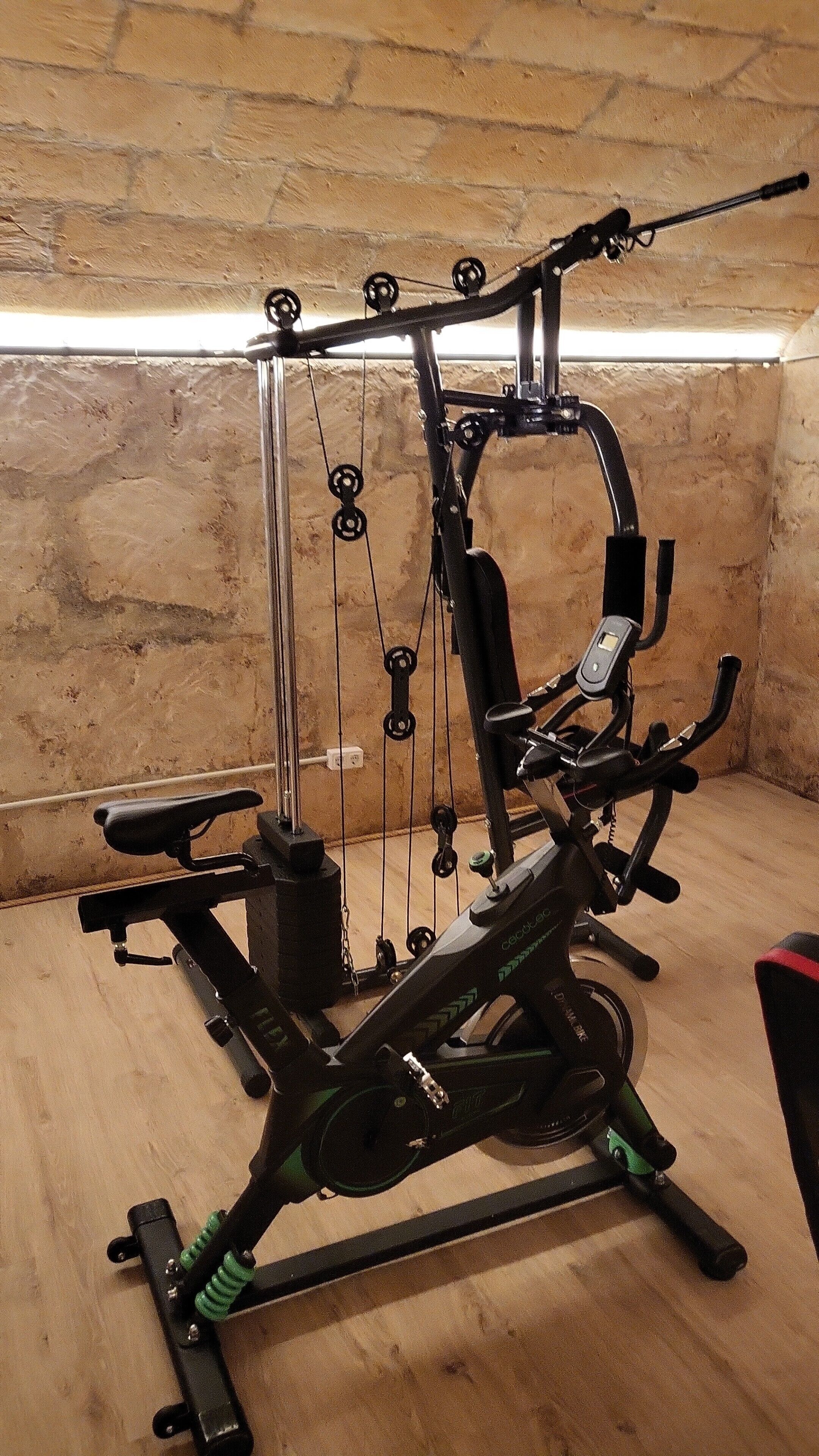 A stationary exercise bike with a digital display, positioned in a room with a brick wall and wooden floor.
