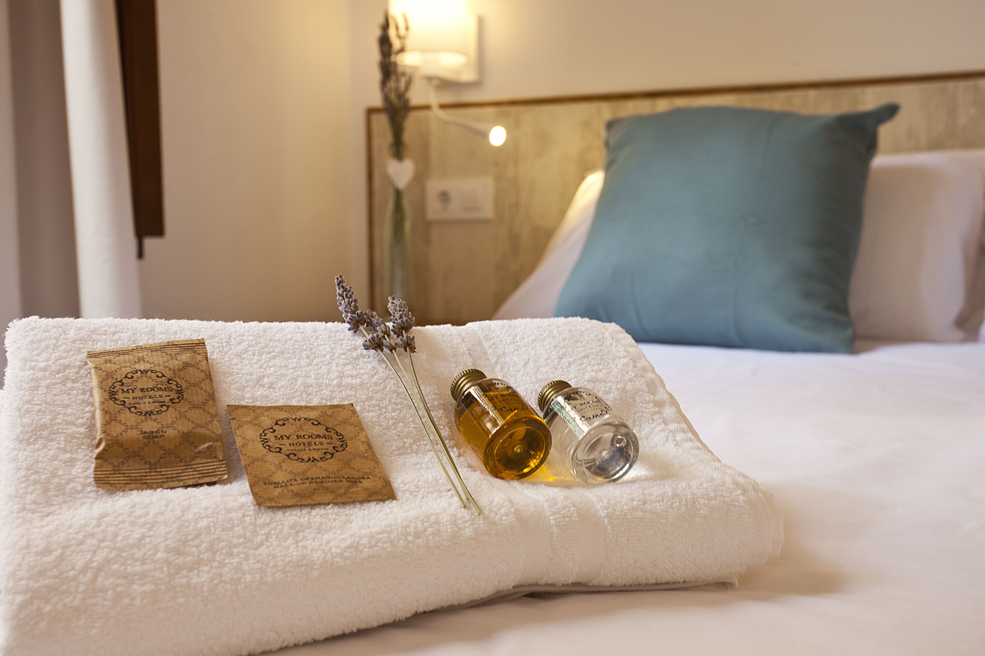 Una cama bien hecha con una toalla blanca, dos botellas pequeñas y dos bolsas de papel marrón.