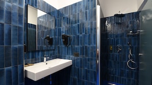 A modern bathroom with blue tiles, a white sink, a mirror, and a shower area.
