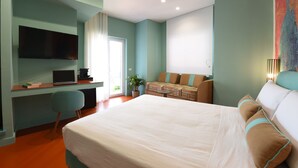 A modern hotel room with a large bed, a desk with a laptop, a flat-screen TV, and a sofa.
