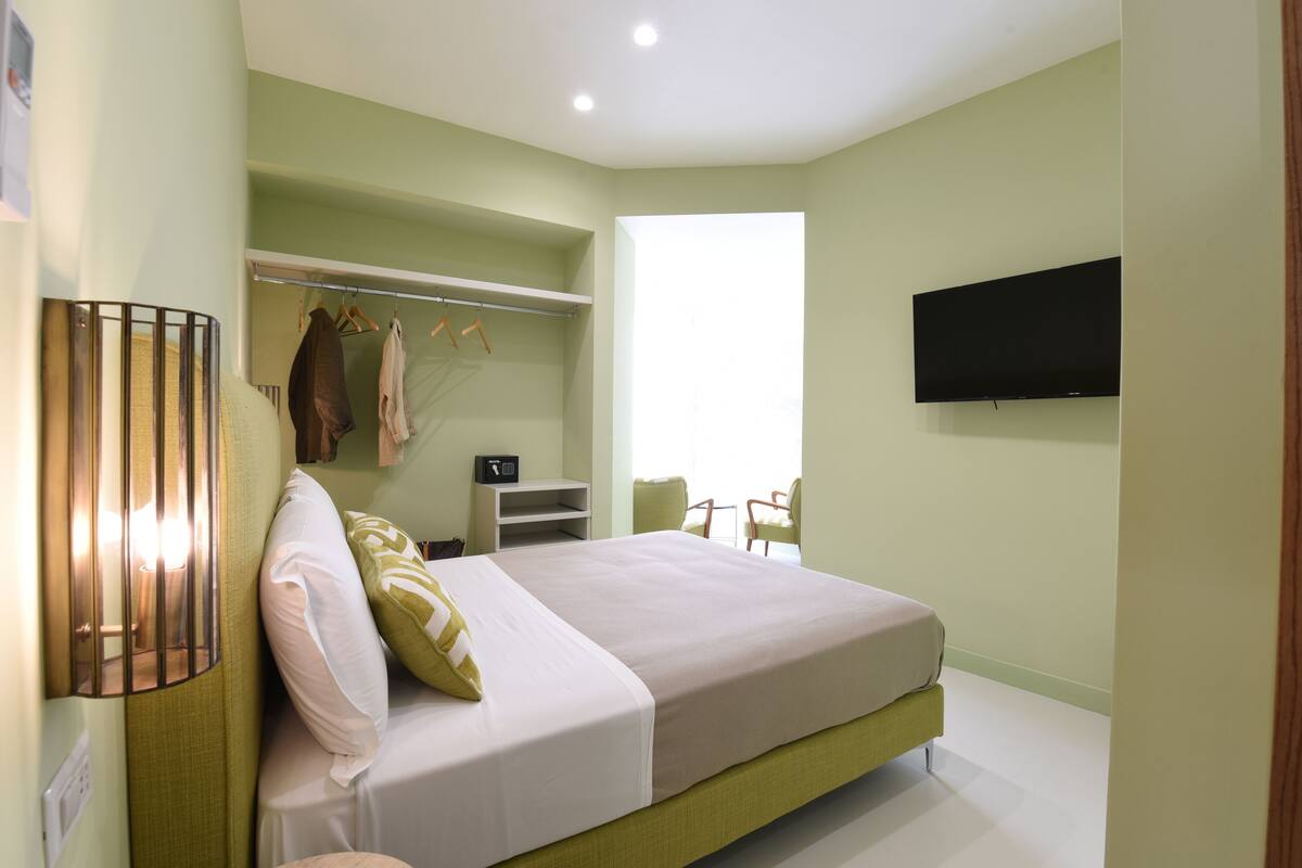 Un dormitorio con una cama, televisor montado en la pared, armario y ventana.