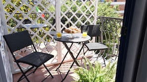 A balcony with a table and two chairs, a small plant, and a view of the surrounding buildings.