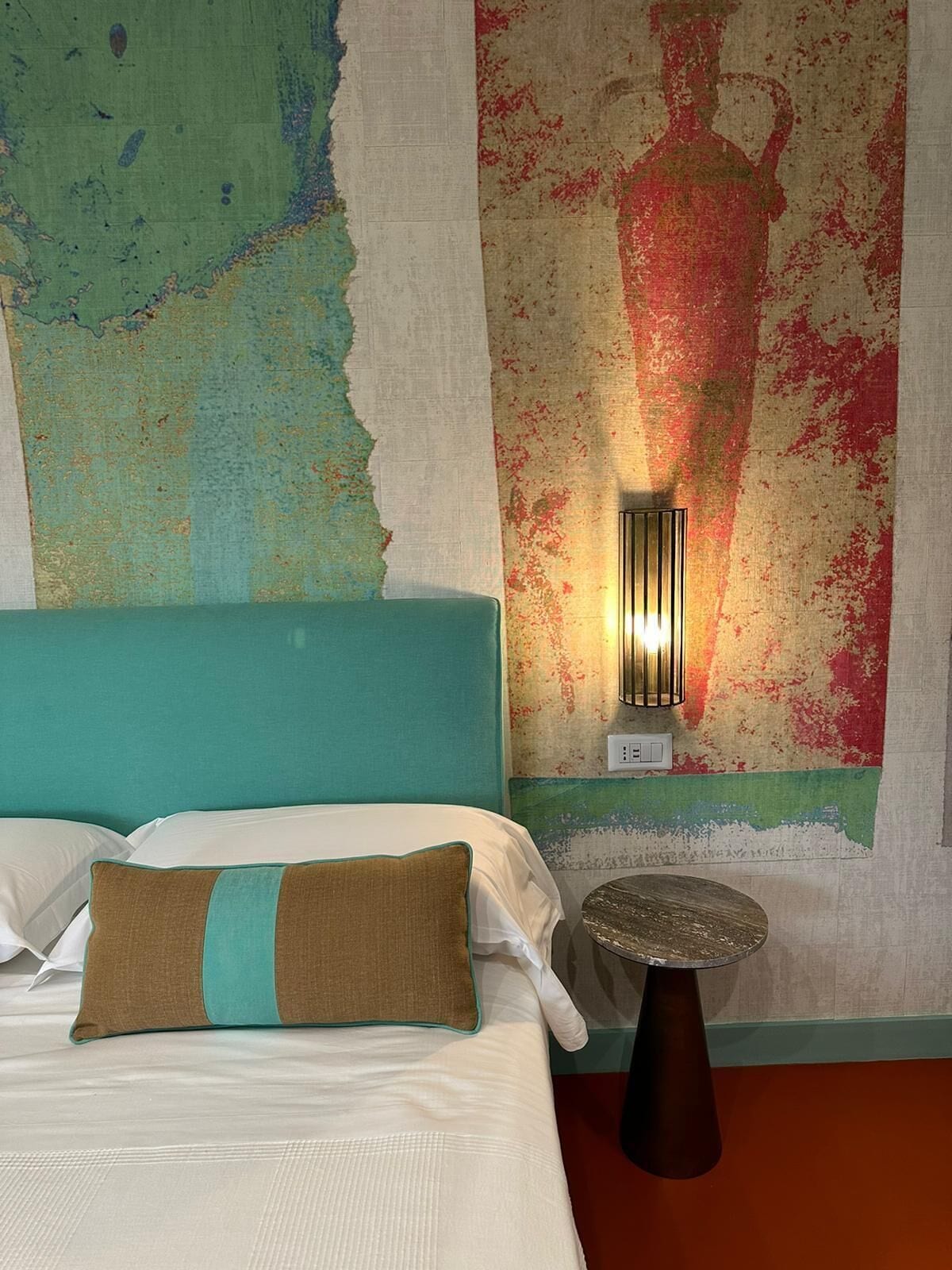 A hotel room with a bed, a nightstand, and a wall with a textured mural.
