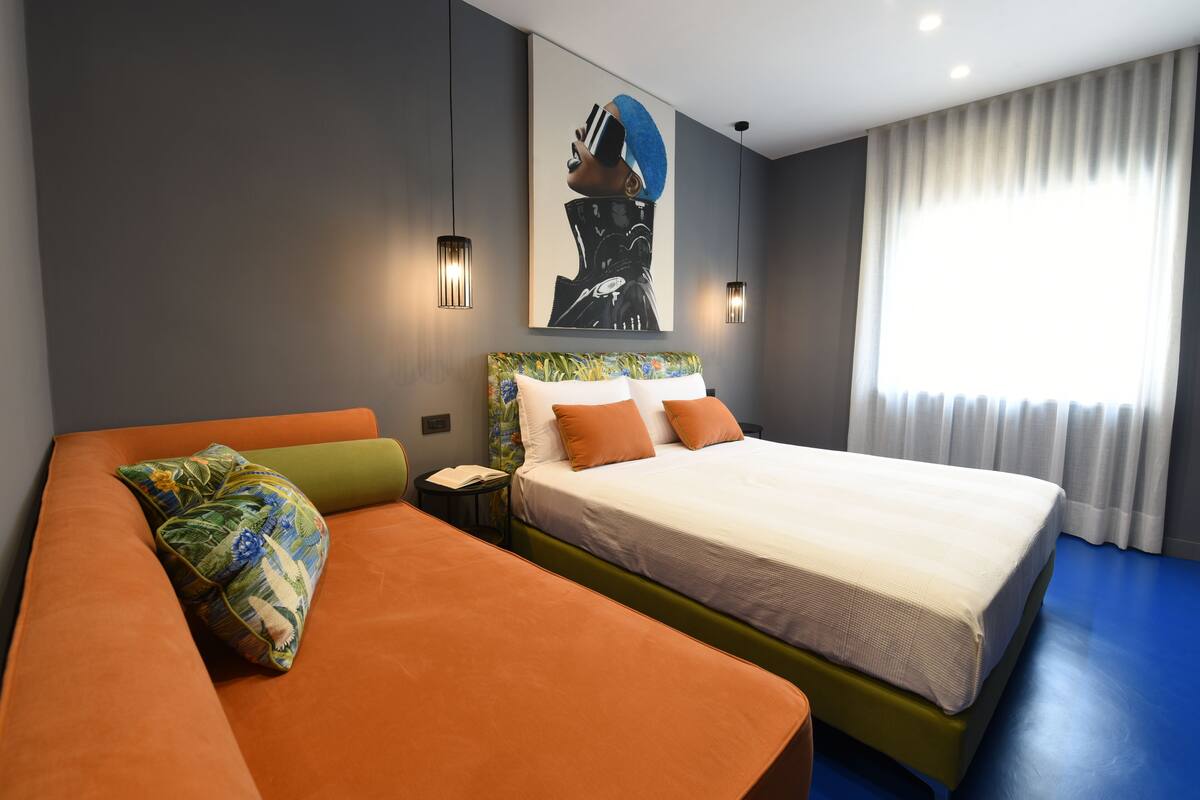 Una habitación de hotel moderna con una cama grande, un sofá naranja y una mesita de noche.