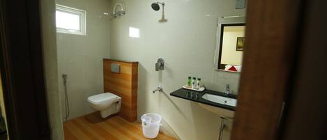 A bathroom with a toilet, shower, sink, and a bucket on the floor.