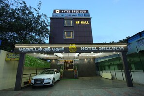 L’hôtel Sree Devi, avec son panneau indicateur, un escalier menant à l’entrée et une voiture garée.
