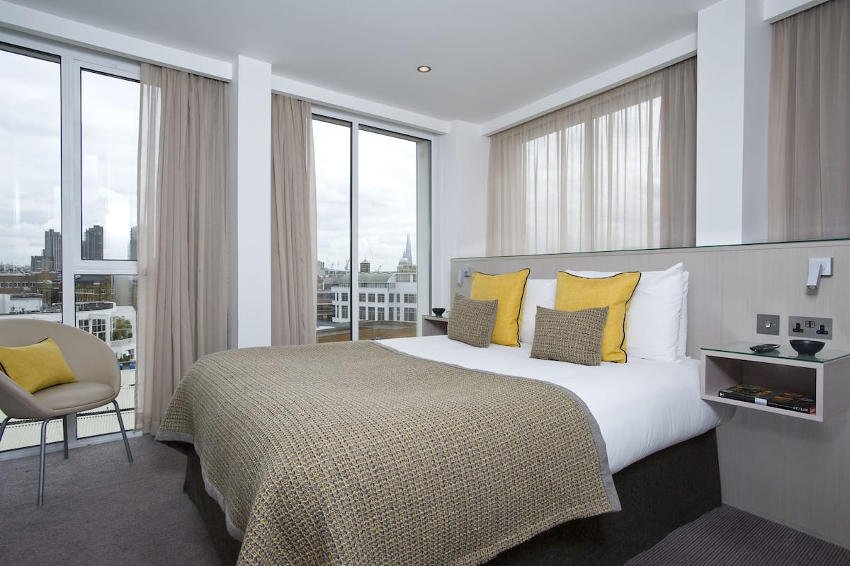 Una habitación de hotel moderna con una cama grande, una mesita de noche de vidrio y una silla.