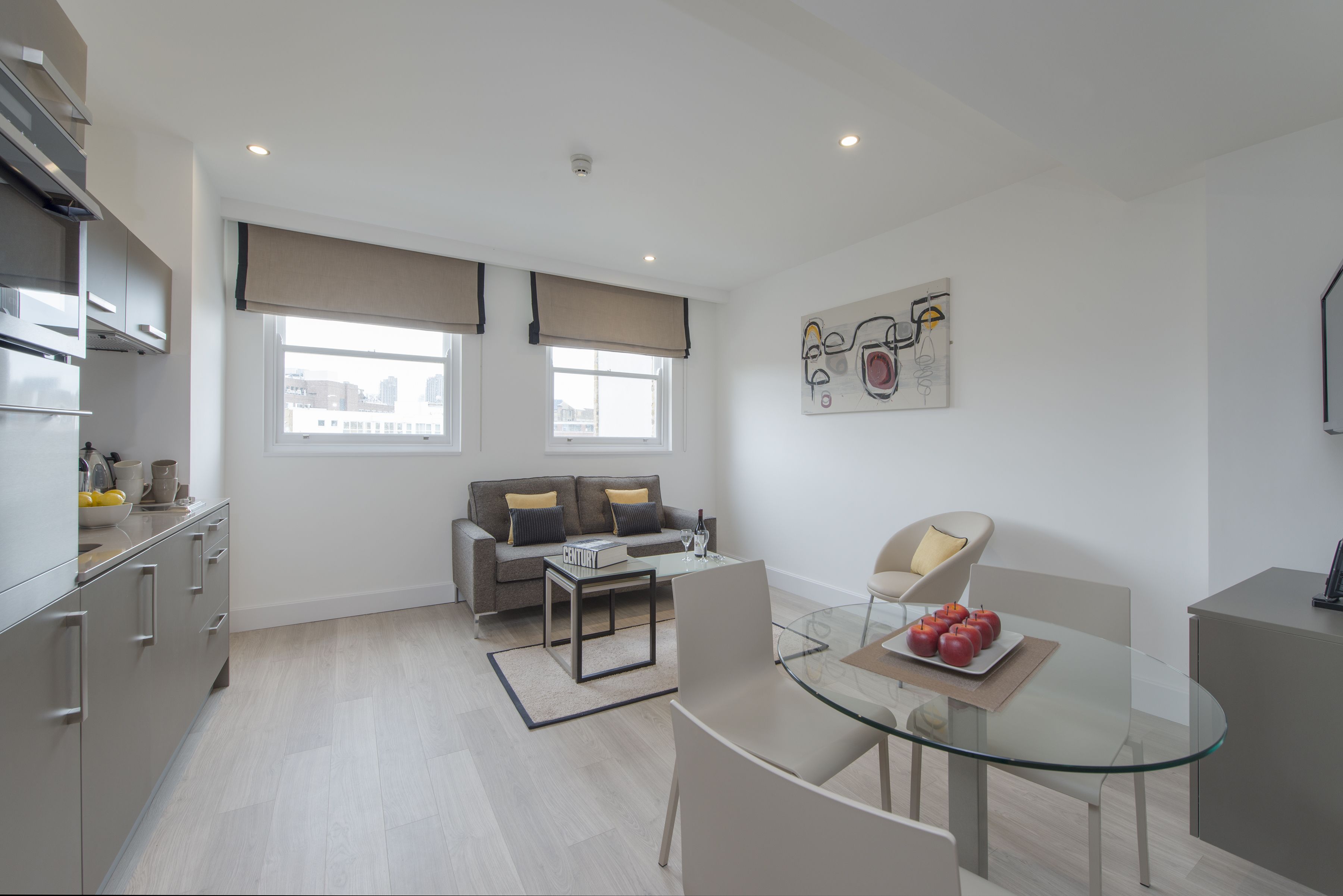 A modern kitchen with a dining area, a sofa, and a glass table with a fruit plate.