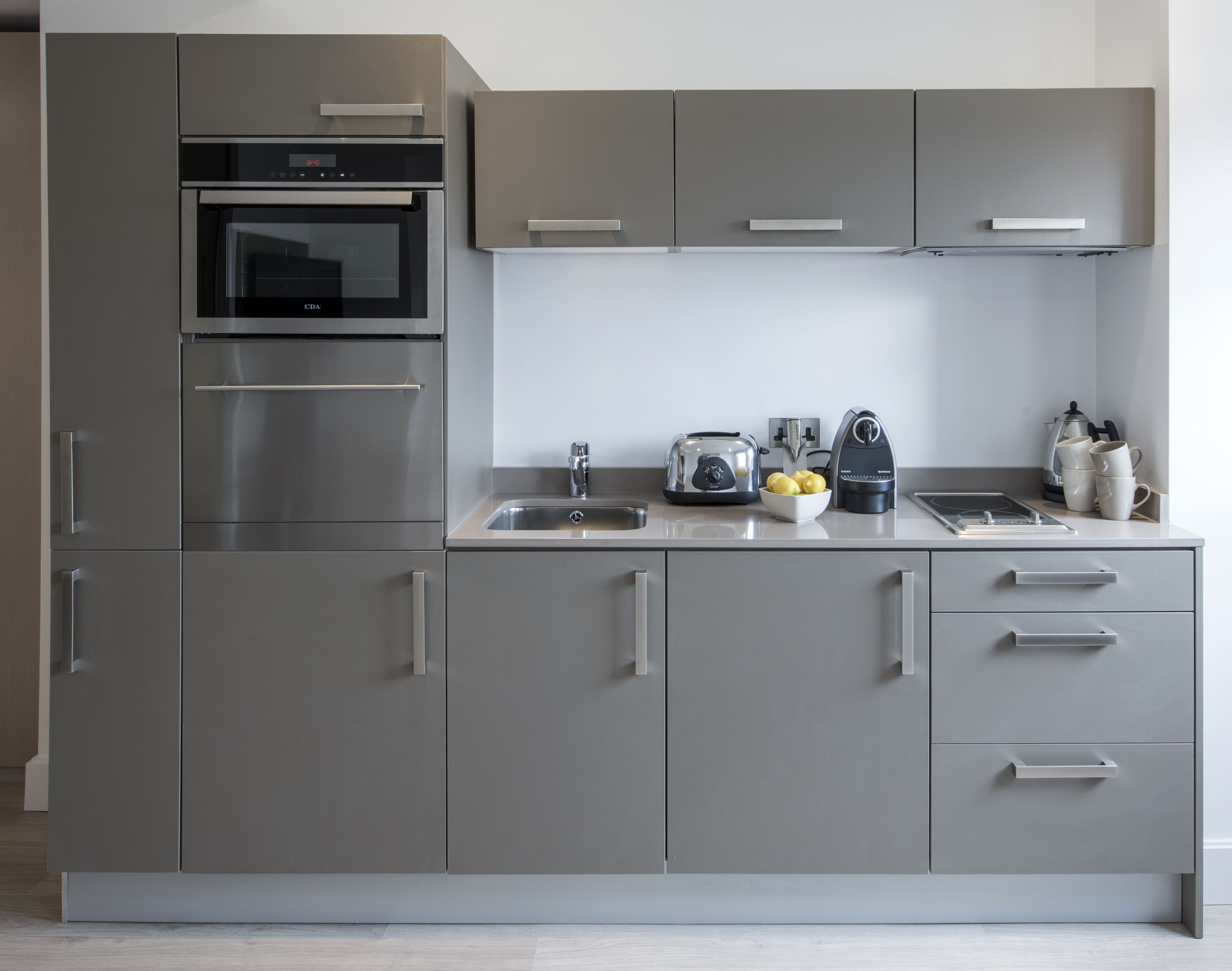 A modern kitchen with stainless steel appliances, a built-in oven, a toaster, and a kettle on the countertop.