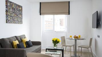 A modern living room with a grey sofa, yellow cushions, a glass coffee table, and a dining area with a small round table and chairs.