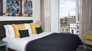 A hotel room with a large bed, a city view, and a painting on the wall.
