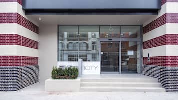 A modern building entrance with a glass door, a sign reading "The Rosebery," and a small garden area with plants.