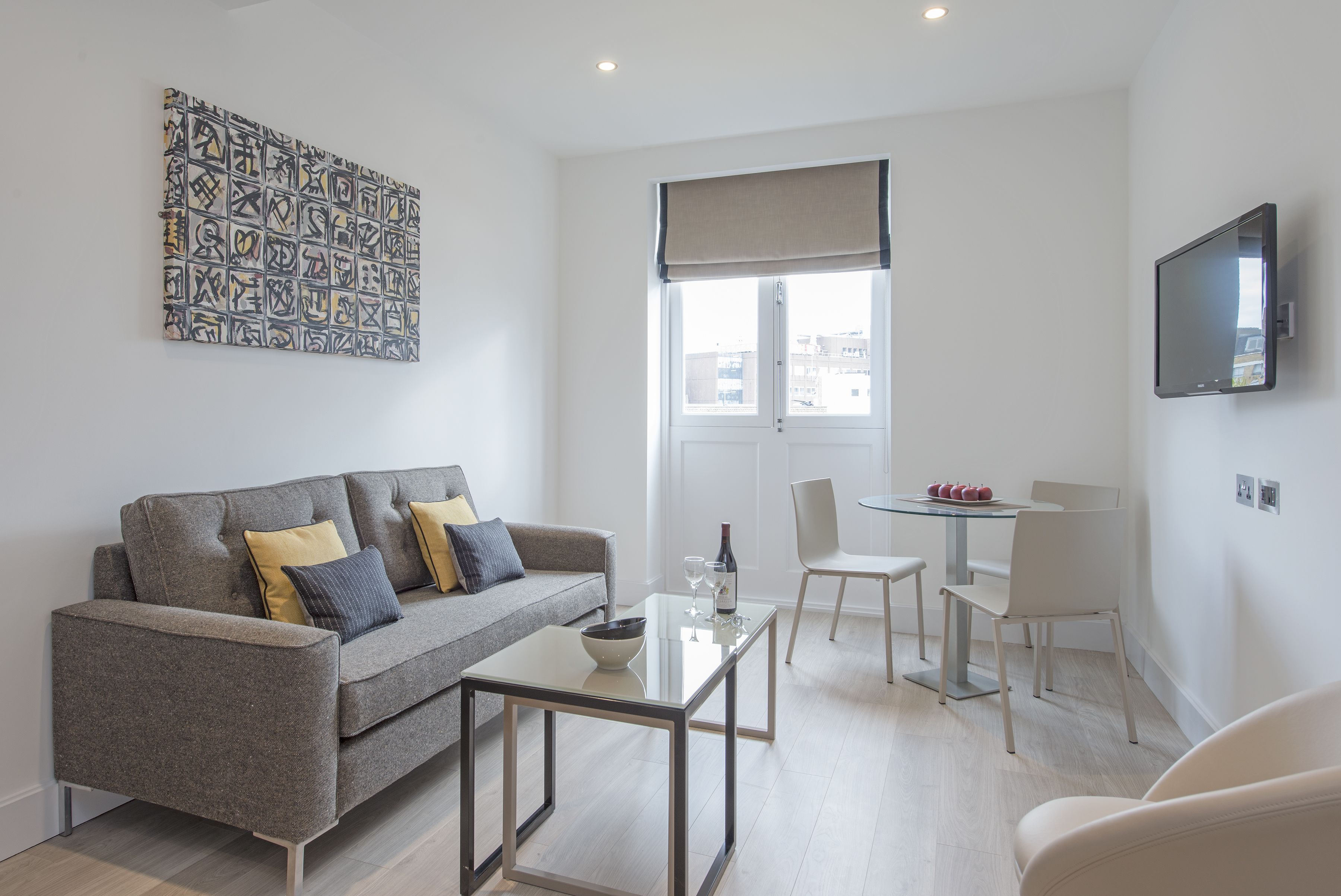 A modern living room with a grey sofa, a glass coffee table, and a dining area with a small table and chairs.
