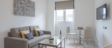 A modern living room with a grey sofa, a glass coffee table, and a dining area with a small table and chairs.