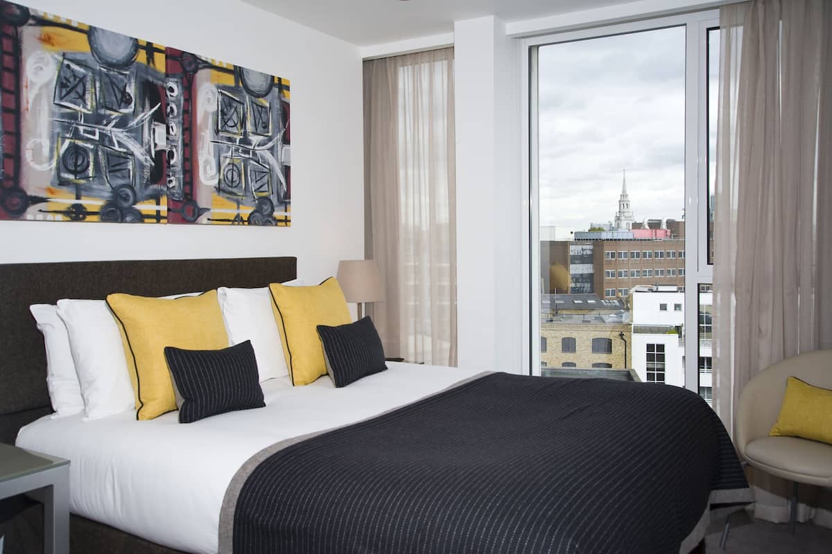 Una habitación de hotel con una cama grande, vista a edificios y un cuadro en la pared.