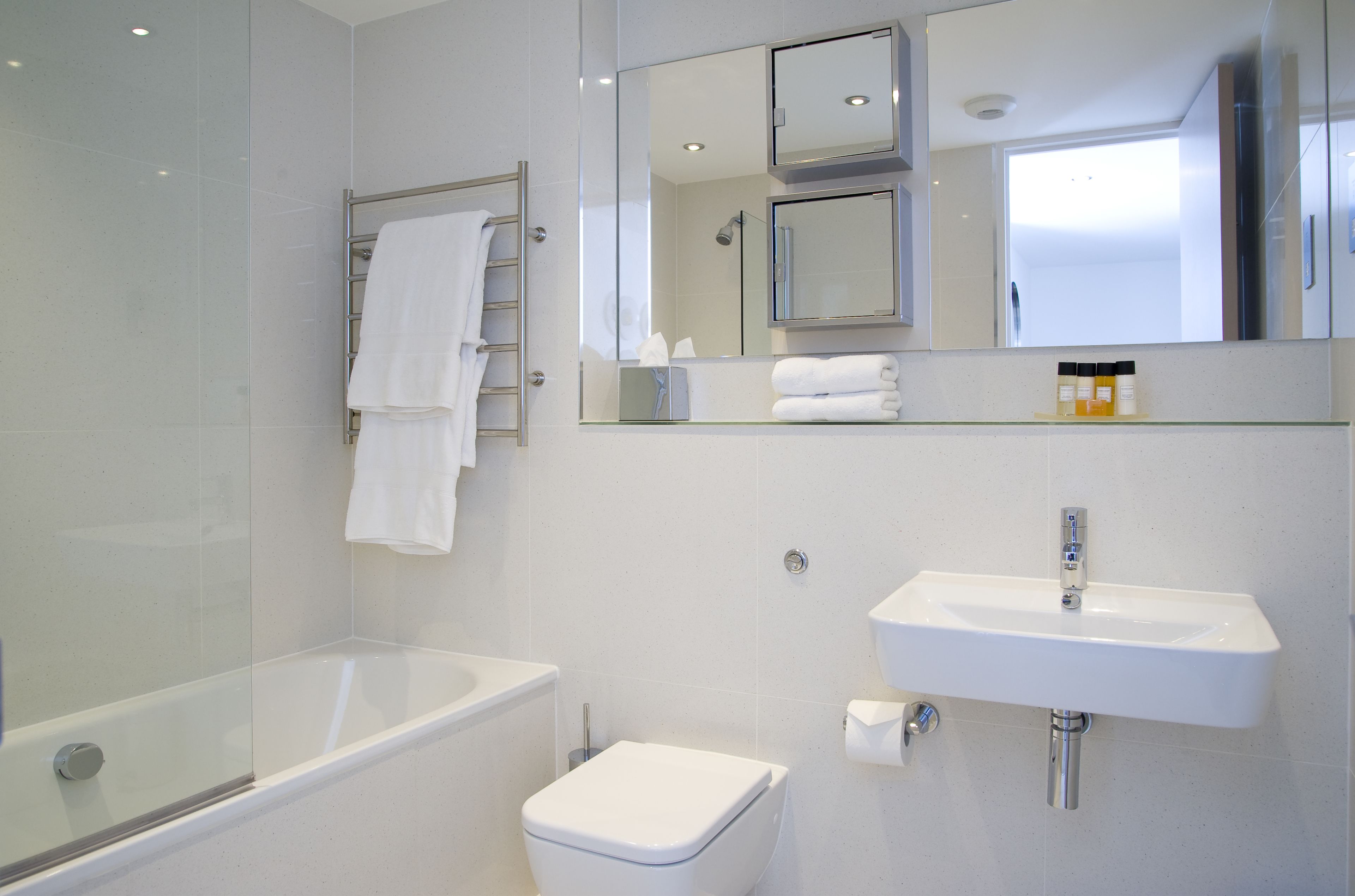 Ein modernes Badezimmer mit einer gläsernen Duschkabine, einer weißen Toilette, einem Waschbecken und einem Spiegel darüber.