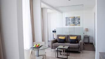 A modern living room with a glass table, a sofa with cushions, a lamp, and a painting on the wall.