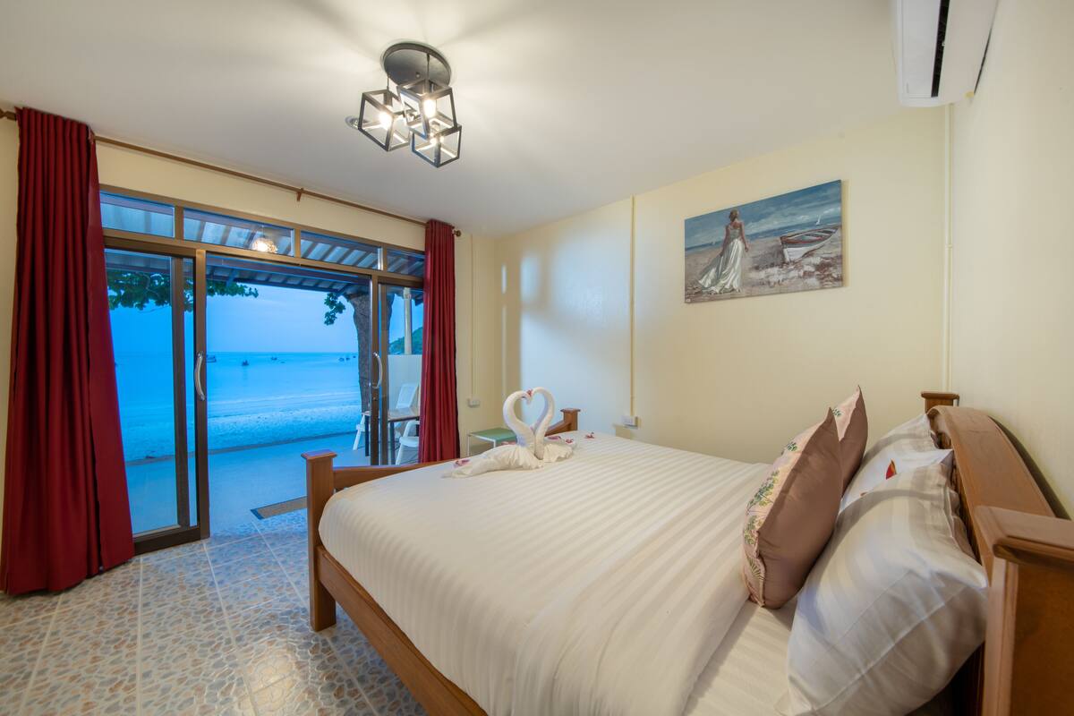 A bedroom with a bed, a painting, and a view of the beach.