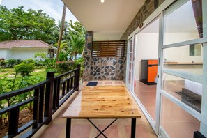A balcony with a wooden table, stone wall, and glass doors leading to a room. - Thong Nai Pan Beach Residence (Ko Pha-ngan)