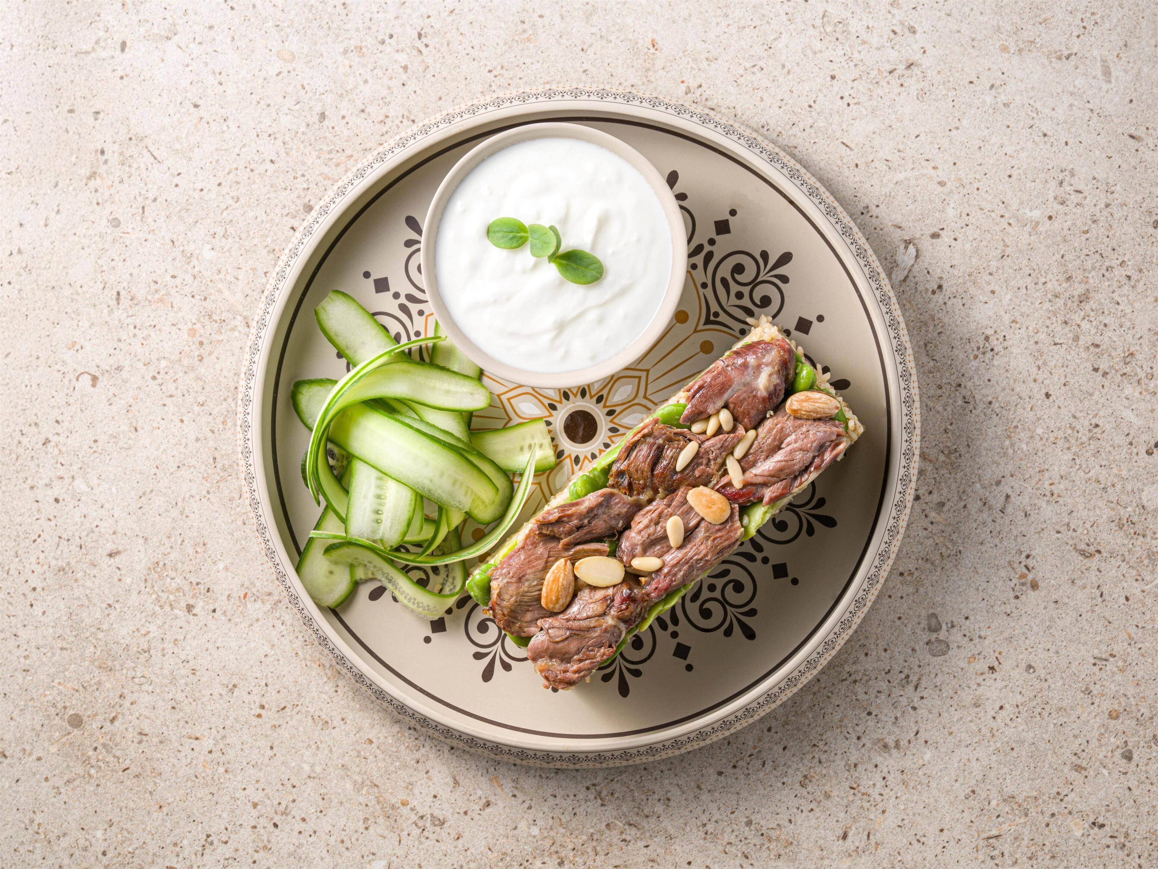 A plate with sliced cucumbers, a meat dish garnished with almonds, and a bowl of yogurt.