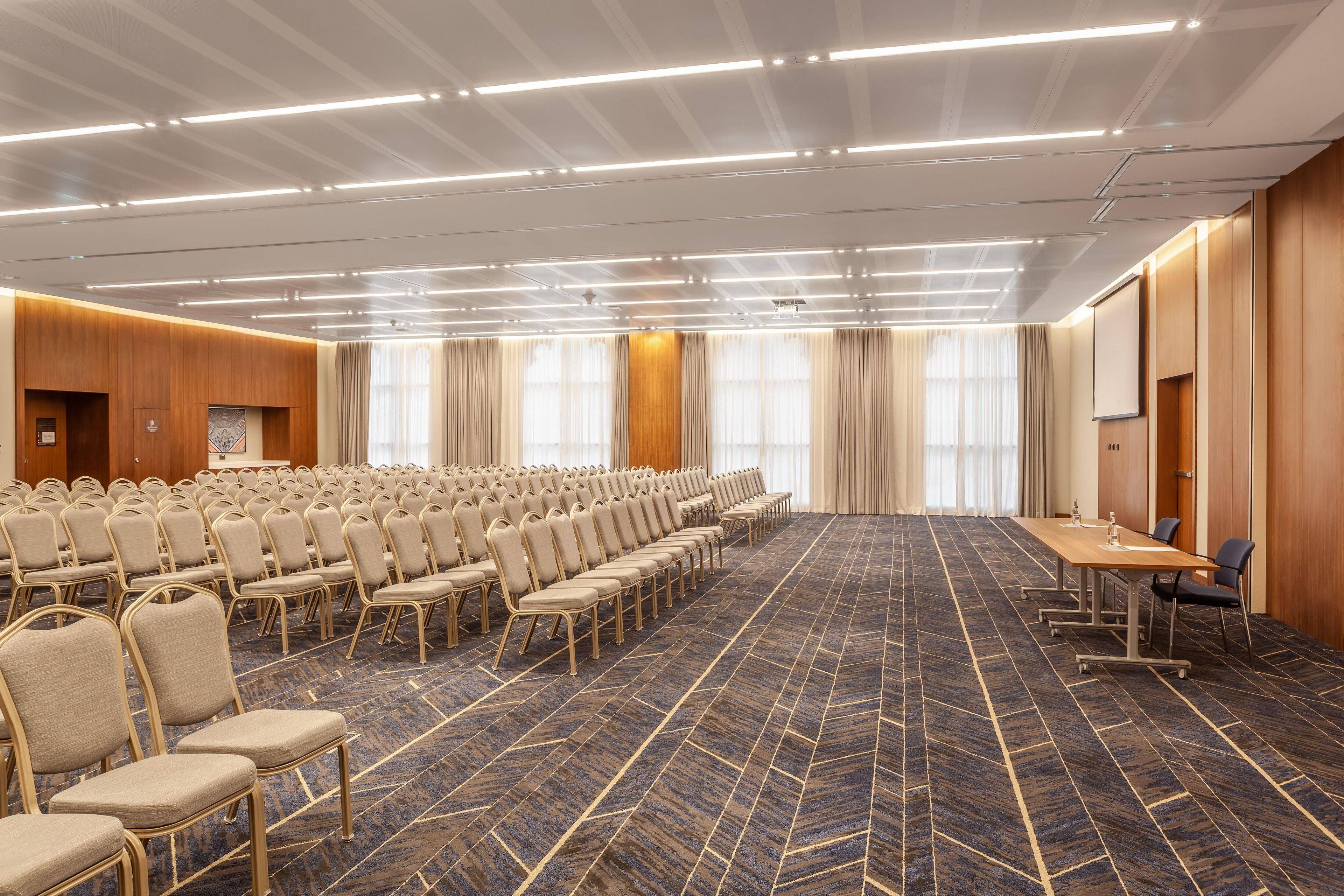 A conference room with rows of chairs, a long table, and a carpeted floor.