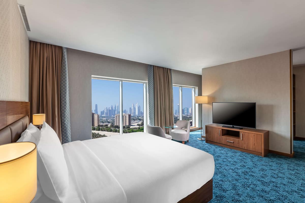 Une chambre d’hôtel avec un grand lit, une télévision, un bureau et une vue sur le paysage urbain.