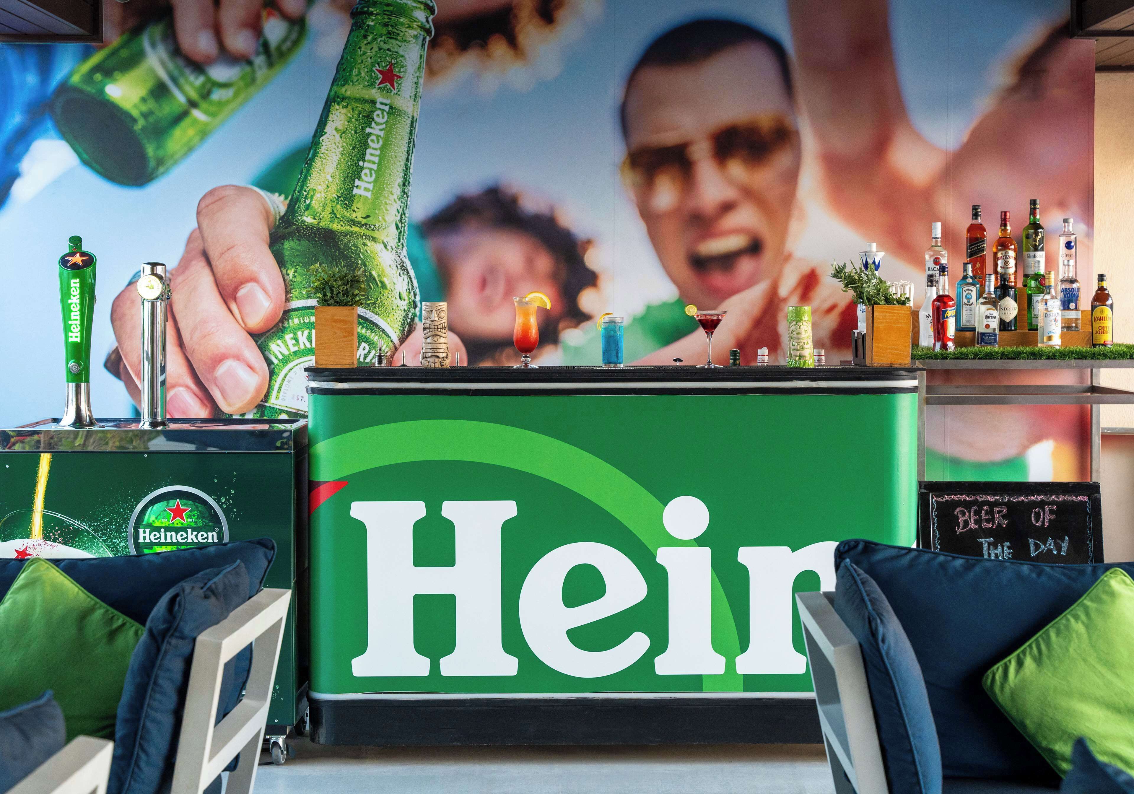 Ein Barbereich mit einem Heineken-Schild, einer Auswahl an Flaschen und einer Tafel, auf der das 'Bier des Tages' steht.