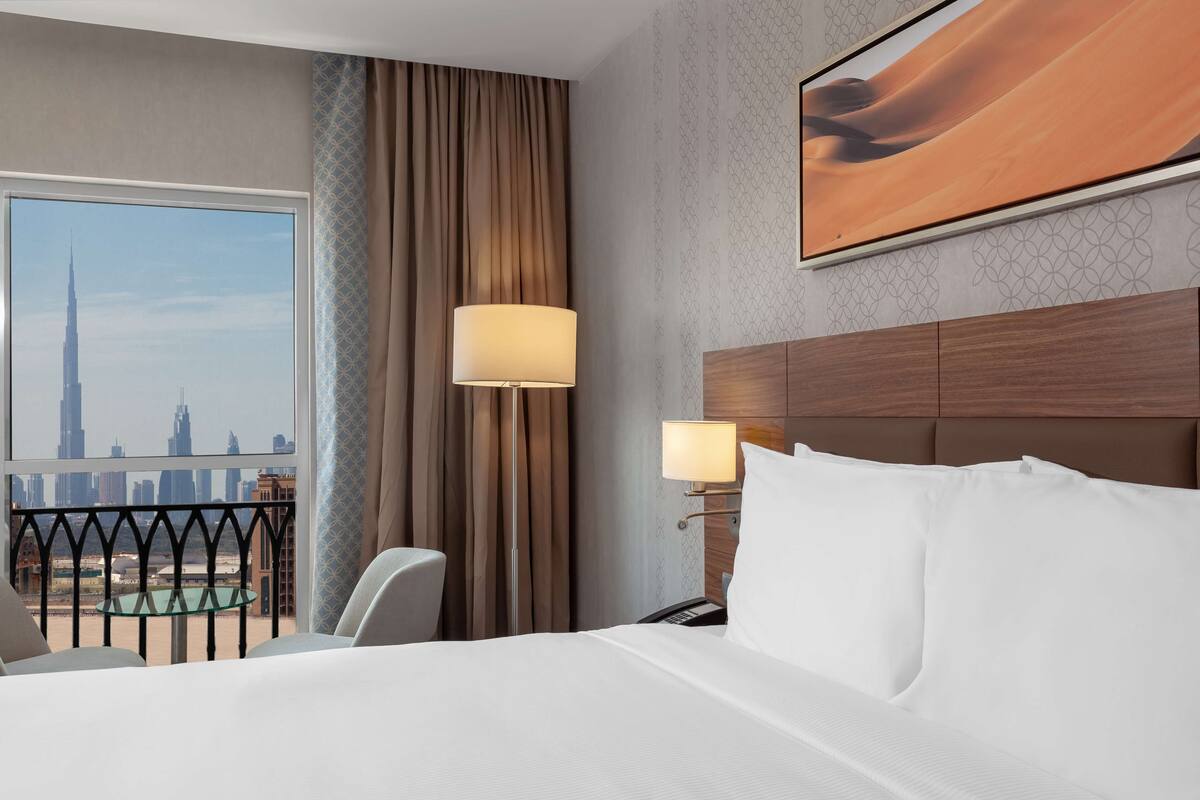 Une chambre d’hôtel avec un grand lit, un bureau, une chaise, une lampe et une vue sur le paysage urbain.