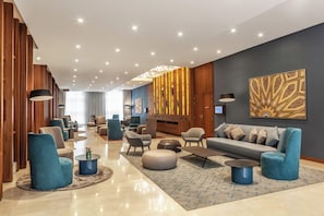 Un moderno vestíbulo de hotel con zona de estar, una recepción y una gran obra de arte en la pared.