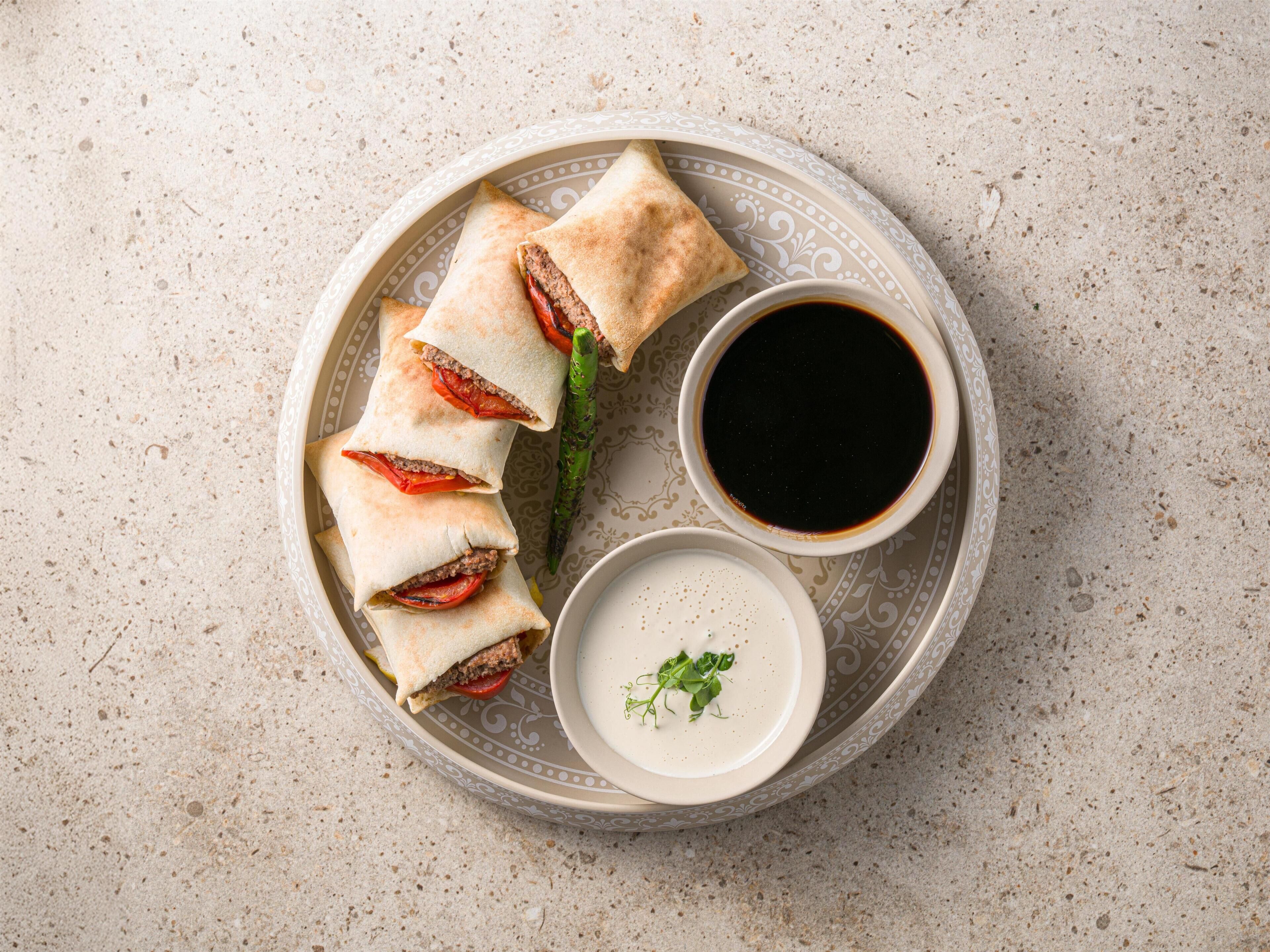 A plate with food items and a cup of sauce.