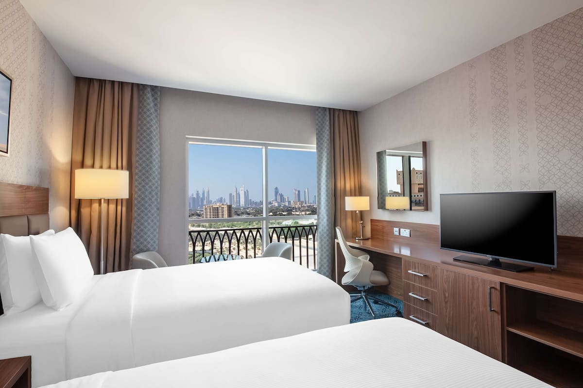 Une chambre d’hôtel avec un grand lit, un bureau avec une télévision et une vue sur le panorama de la ville.