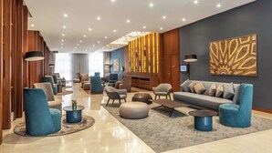Eine moderne Hotelhalle mit großzügigem Design, die verschiedene Sitzbereiche, einen zentralen Couchtisch und eine große Couch bietet.