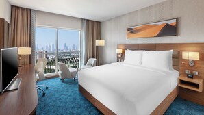 Ein Hotelzimmer mit einem großen Bett, einem Schreibtisch, einem Stuhl und Blick auf eine Stadtansicht.