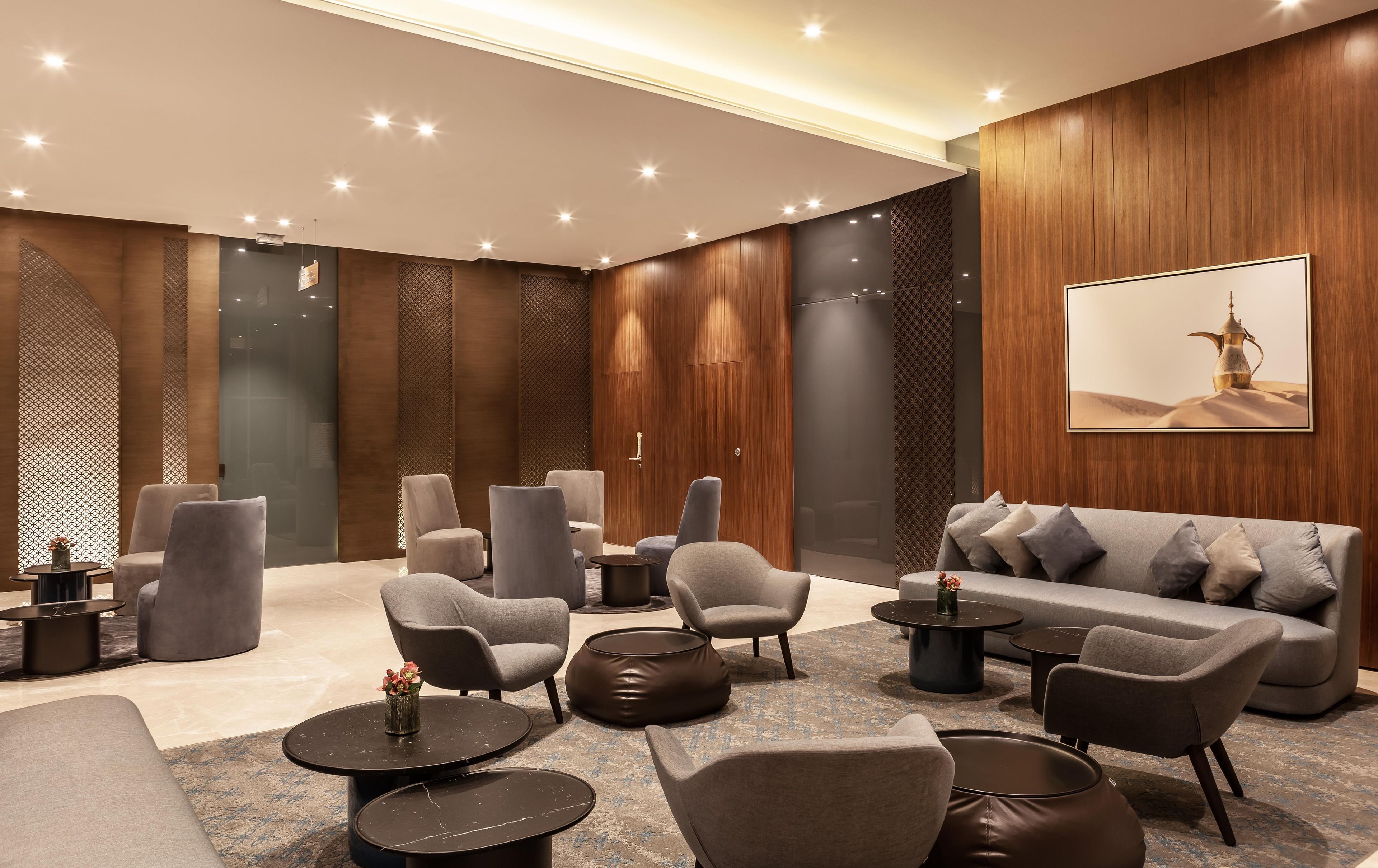 A modern lounge area with sofas, chairs, and round tables, featuring a wooden wall and a framed picture.
