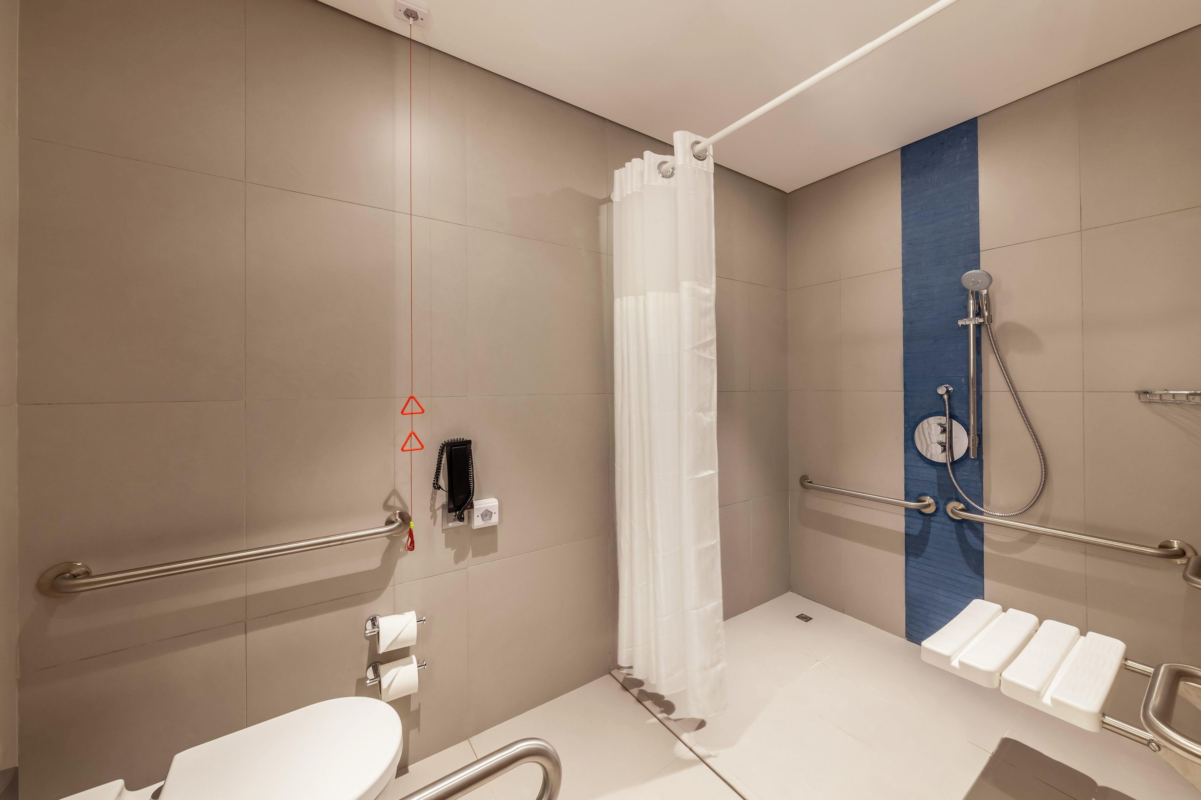 Une salle de bain moderne équipée d’une douche, de toilettes et de barres d’appui.