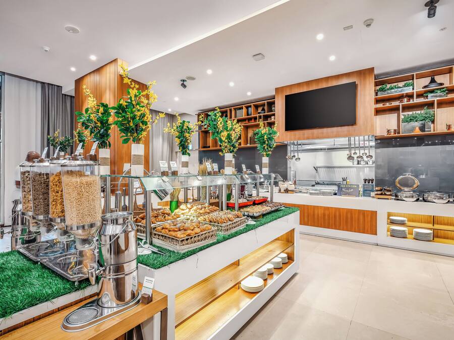Un buffet de desayuno moderno con diversas opciones de comida, una estación de café y plantas decorativas.