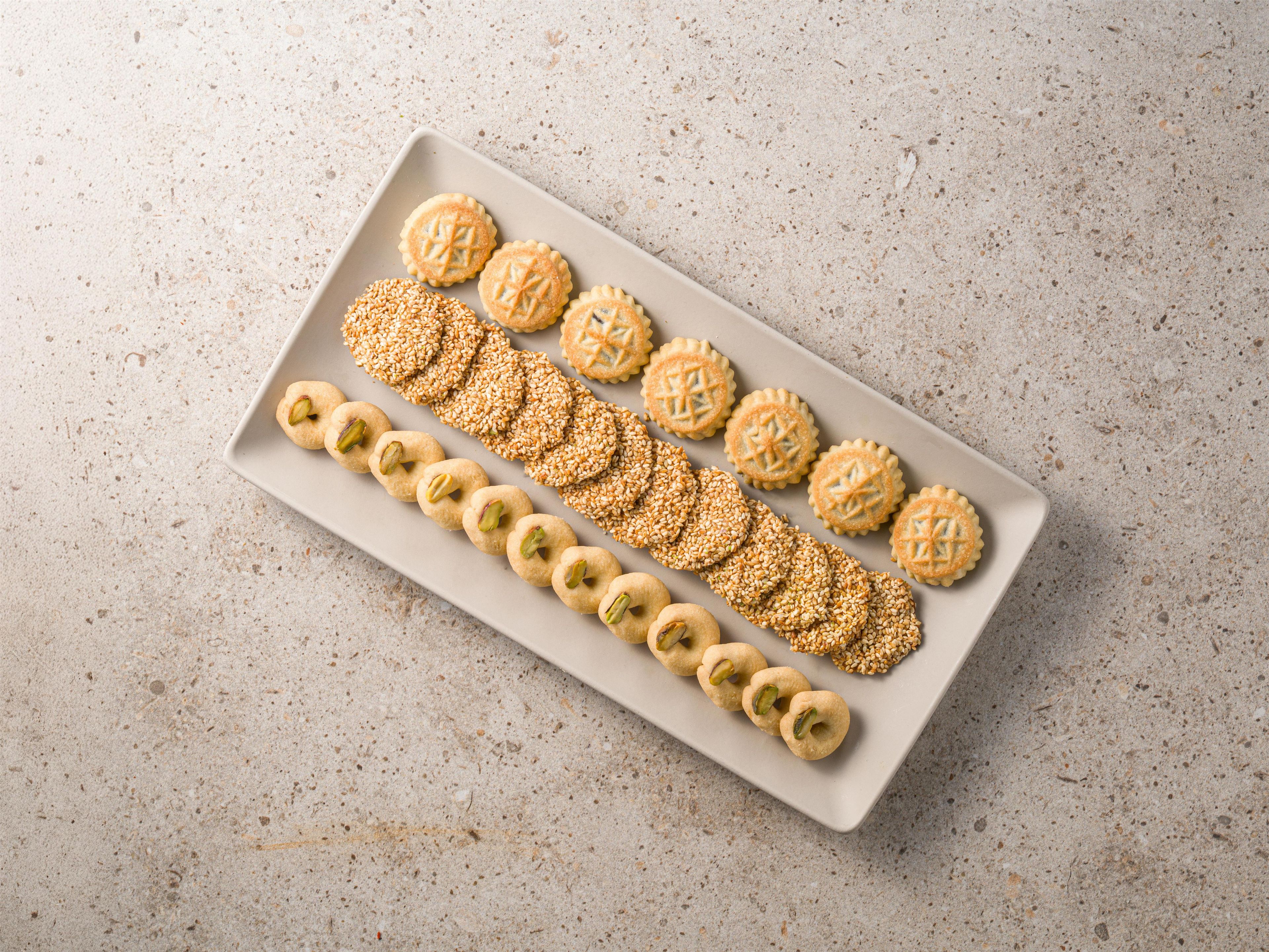 Een rechthoekig bord met verschillende koekjes en sesamzaadjes op een gereliefd oppervlak.