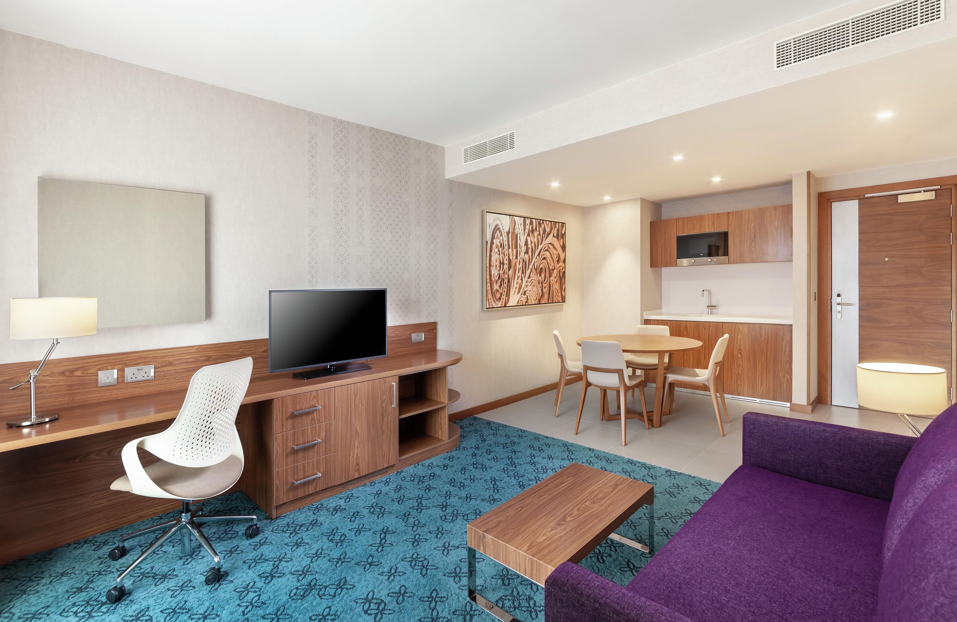 Une chambre d’hôtel équipée d’un bureau, d’une chaise, d’une télévision, d’une table à manger, de chaises et d’un canapé.