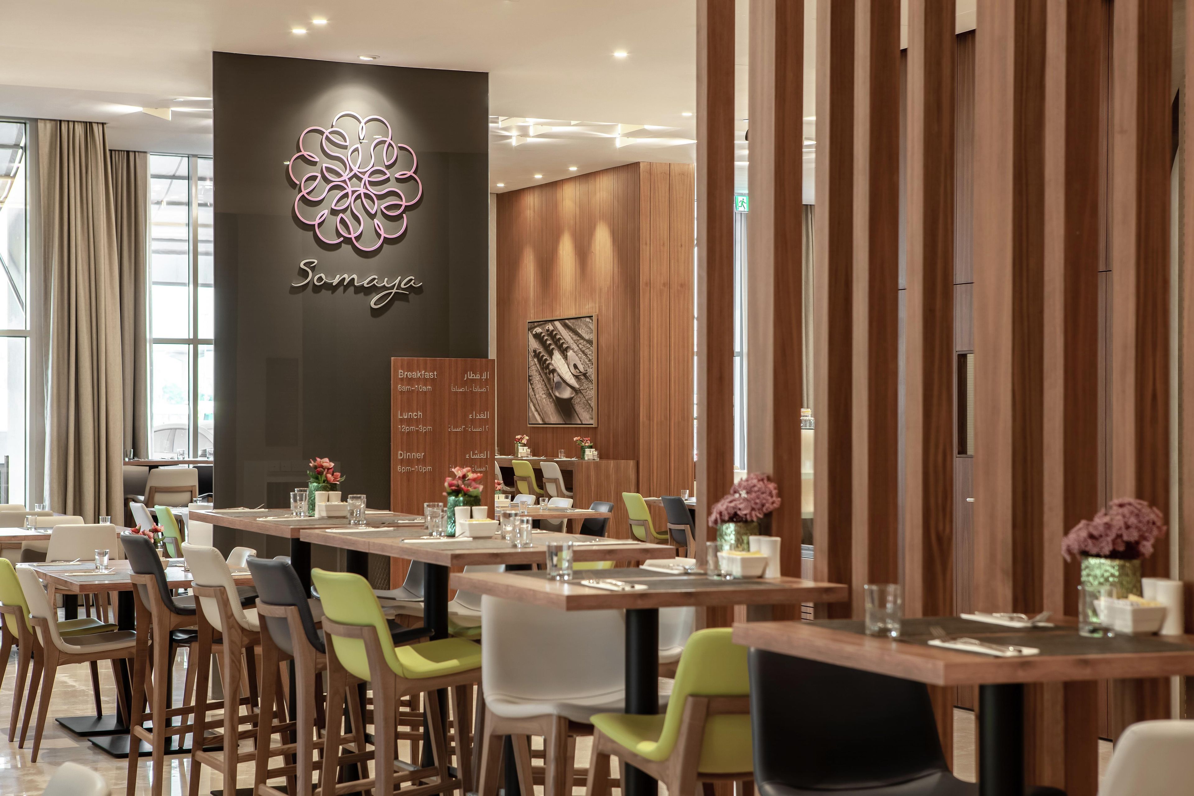 Un espace repas moderne avec des tables et des chaises en bois, un mur décoratif orné d’un logo et un panneau affichant le menu.